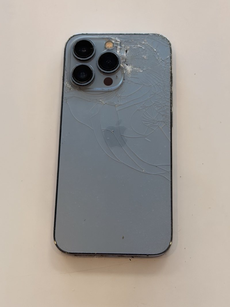 A blue phone with its rear glass panel shattered, photographed on the bench before repair.