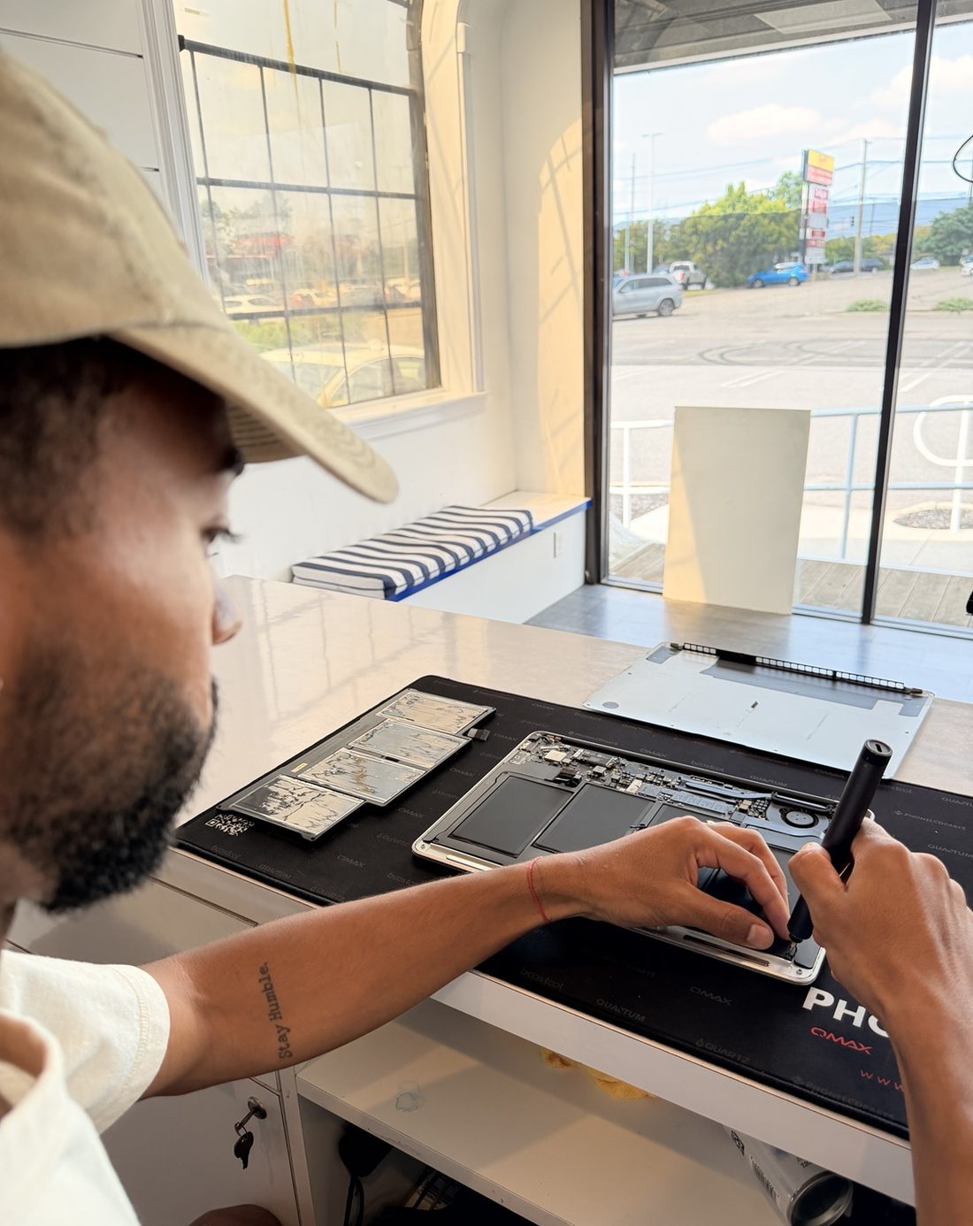 Benjamin working on an opened MacBook at the repair bench, with the shop window behind him.