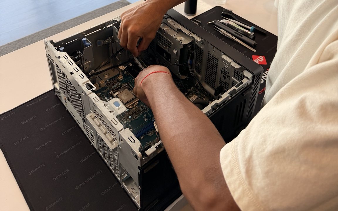 Hands working inside an opened desktop computer on the repair bench.