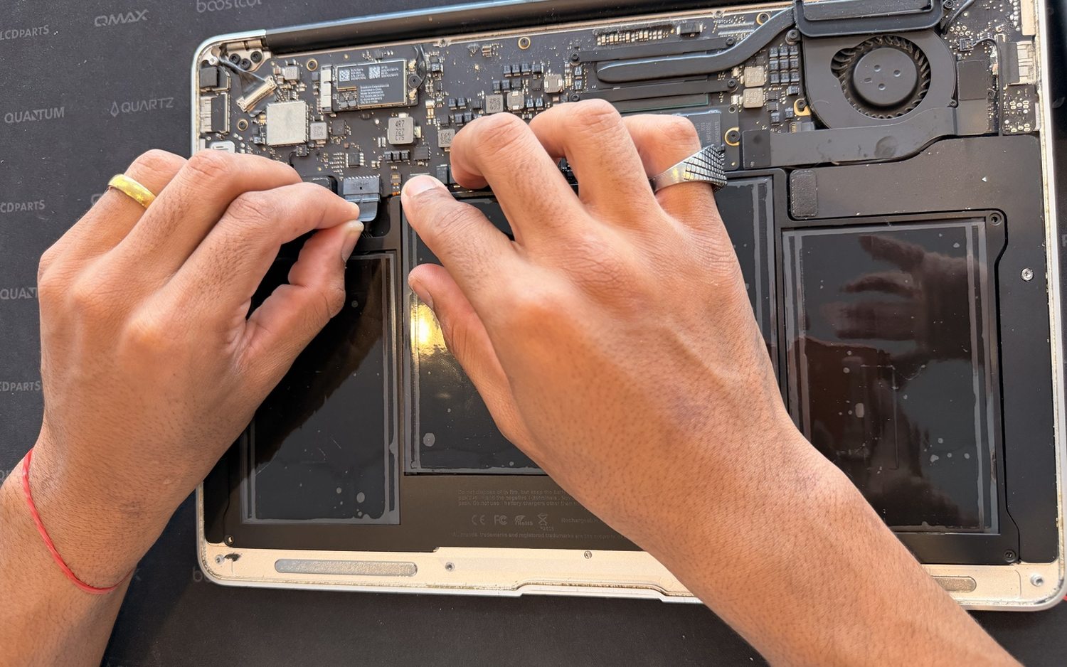 Hands working on the internal connectors of an opened MacBook on the repair bench.