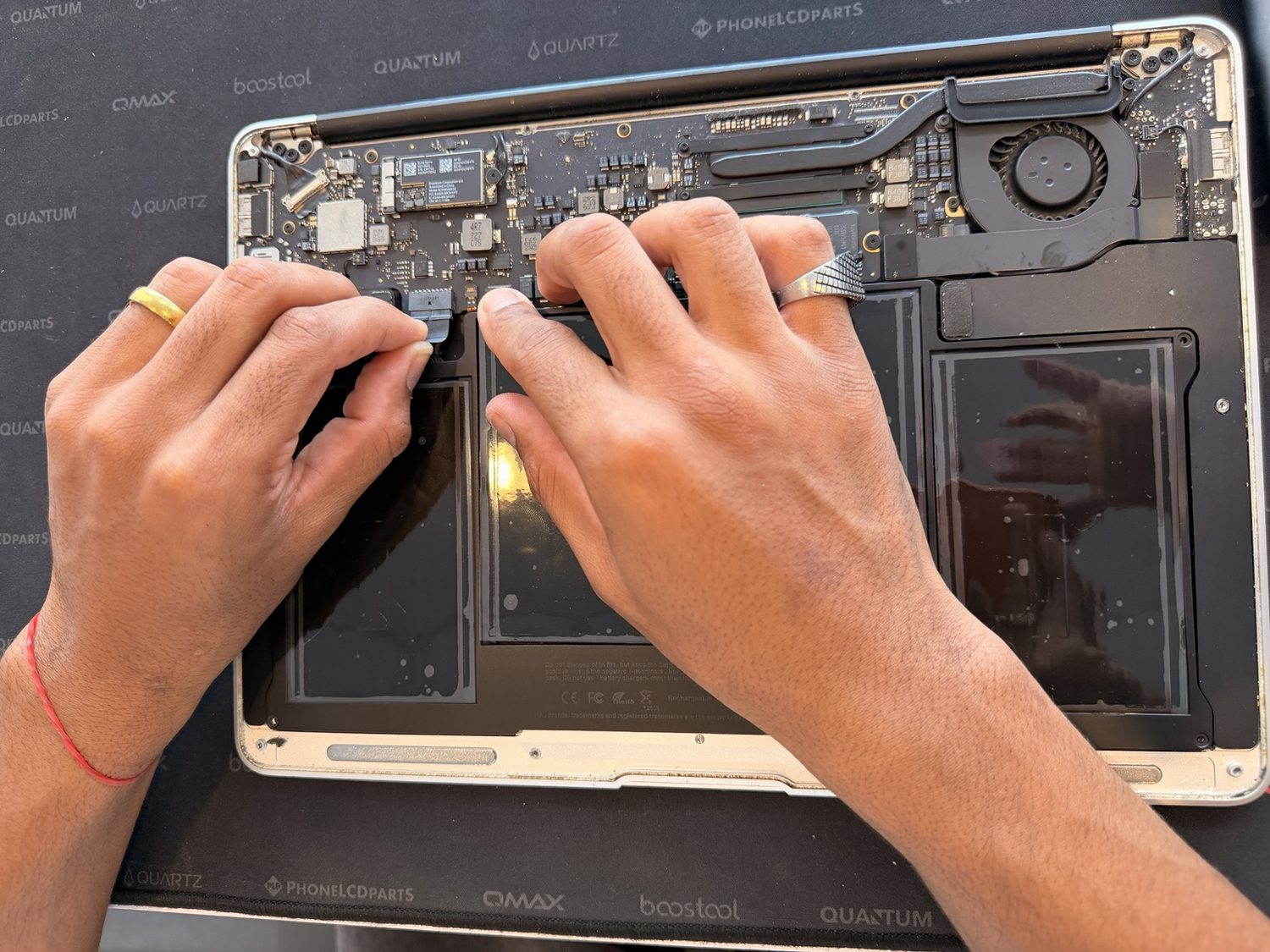 Two hands disconnecting a ribbon cable inside an opened MacBook on the repair bench.
