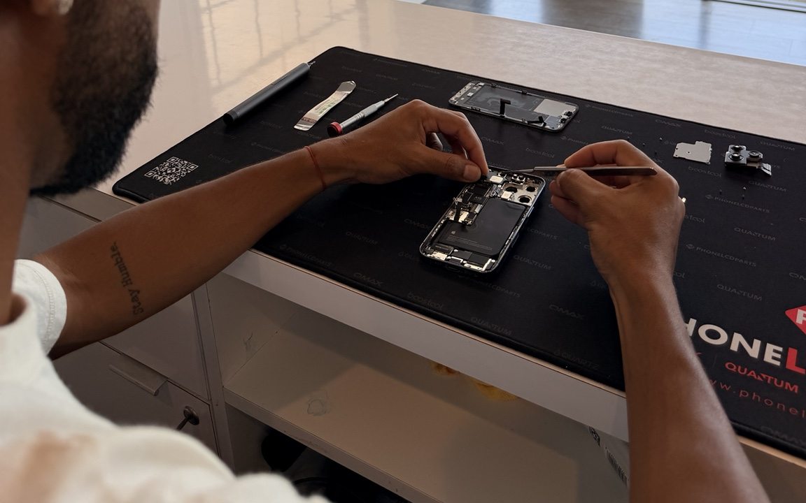 A smartphone opened on the repair bench with tools and its internal components laid out.