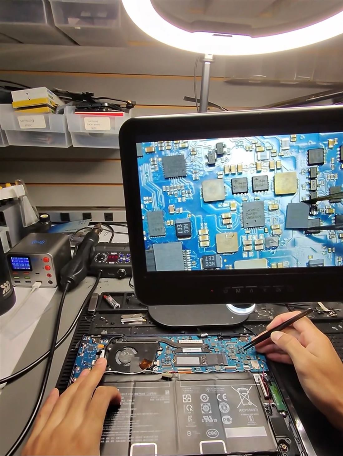 A laptop circuit board positioned under an inspection microscope on the repair bench.